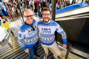 Two men post in BART holiday sweaters.