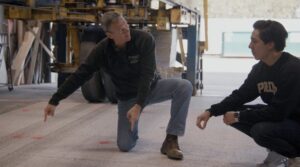 Two men squat to examine slab of concrete pavement in lab.