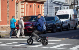 Man on e-bike crosses street.