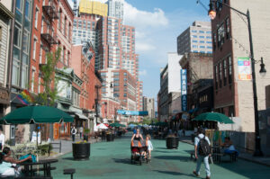 Woman pushes stroller and people walk along pedestrian plaza in Jersey City, NJ.