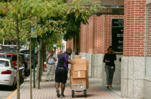 FedEx worker pushes handcart full of packages along sidewalk.