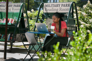 Woman sits at laptop with coffee in Newark's Military Park.
